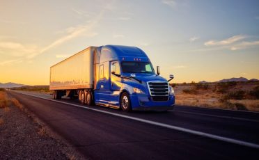 Large semi truck hauling freight on the open highway in the western USA under an evening sky.